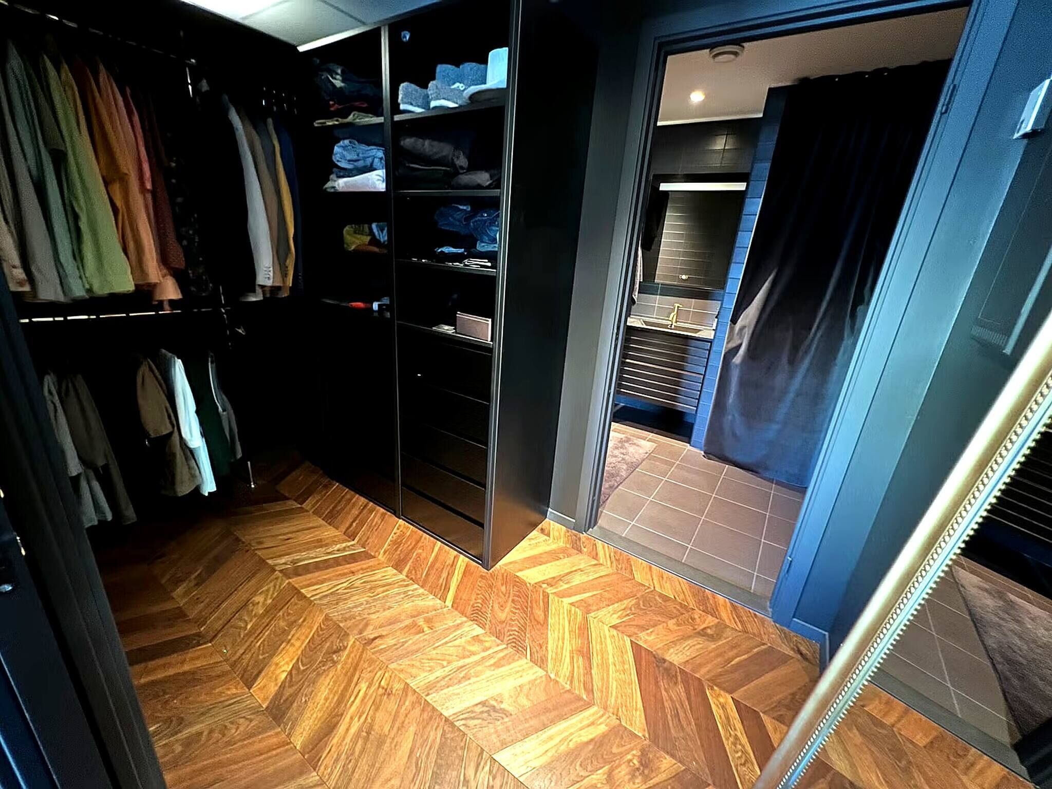 A walk-in closet with wooden flooring and shelves for shoes and folded clothes.