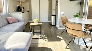 A modern living space with a sofa, a small table with a plant, a TV mounted on the wall, and a dining area with chairs and a table. - Stay on a luxury houseboat at Lake Veerse in Wolphaartsdijk. Enjoy a rooftop terrace, private mooring, water sports and Zeeland's nature. (Wolphaartsdijk)