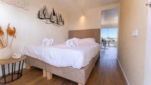 A bedroom with a bed, a wall-mounted artwork, a small table with a vase, and a view through an open door. - Stay on a luxury houseboat at Lake Veerse in Wolphaartsdijk. Enjoy a rooftop terrace, private mooring, water sports and Zeeland's nature. (Wolphaartsdijk)