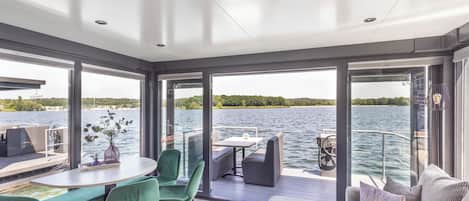 A modern boat interior with a dining area, seating, and a view of the water.