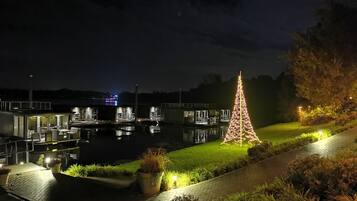 A waterfront property with a large illuminated Christmas tree, a dock with boats, and a building with multiple levels and outdoor seating.