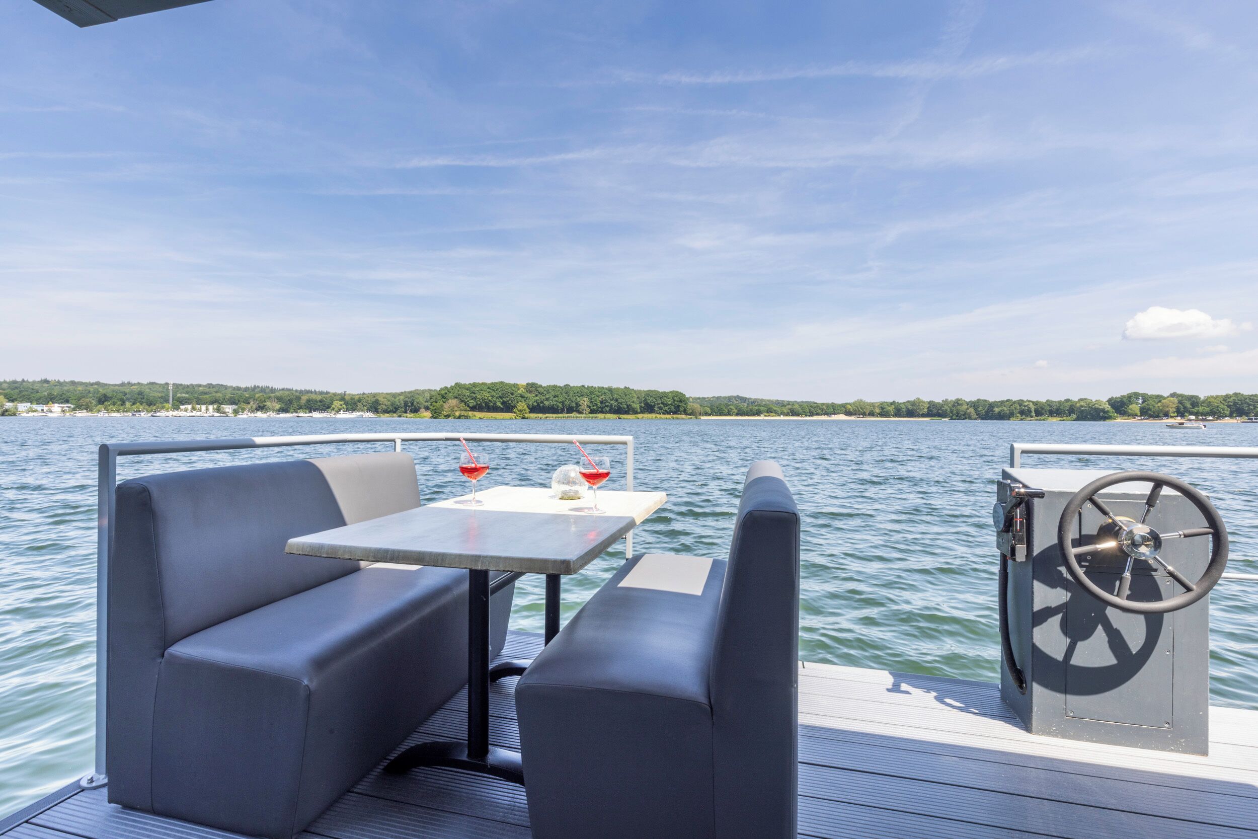 Eine Terrasse mit Tisch, Stühlen, einem Steuerrad und Blick auf Wasser und die Ferne.