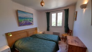 Un dormitorio con dos camas, un escritorio, una silla, una ventana con cortinas, un cuadro en la pared y una lámpara colgante.