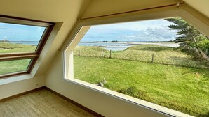 Ein Zimmer mit schrägemausertem Dach, großen Fenstern und Blick auf eine grüne Landschaft mit einem Gewässer.