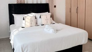 Een netjes opgemaakt bed met witte beddengoed en decoratieve kussens, een zwart hoofdbord en een grote inloopkast met meerdere deuren.