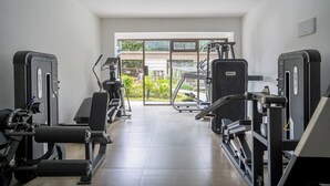 Een sportschool met cardioapparaten, krachttoestellen en uitzicht op groen.