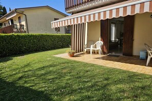 Een huis met een overdekte patio, een gazon en een haag.