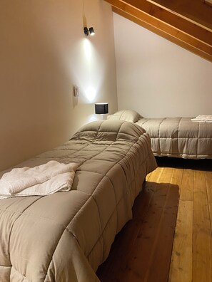 Een slaapkamer met twee bedden, een nachtkastje met lamp, houten vloeren en een schuine plafond.