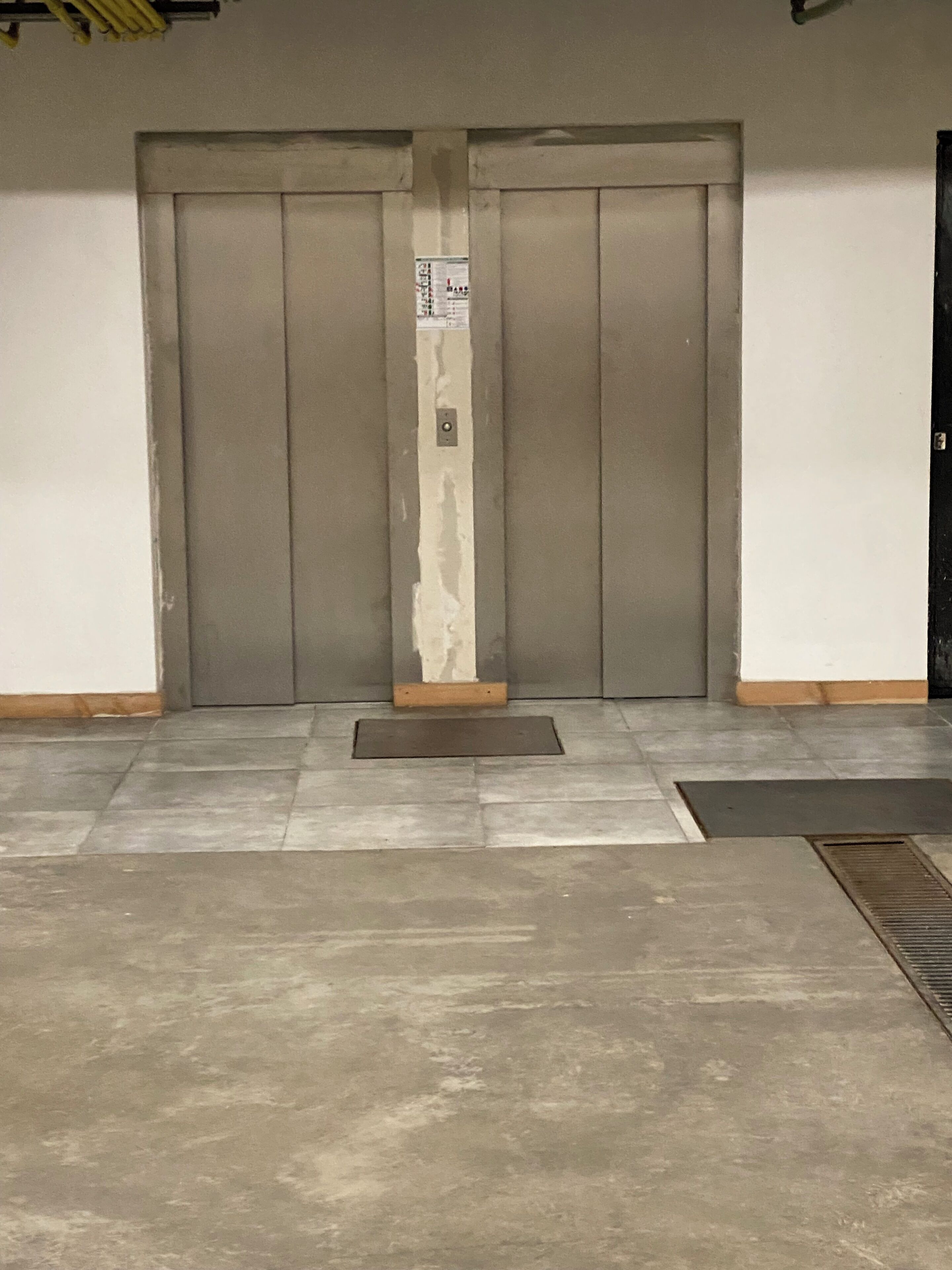 Un conjunto de puertas dobles con un cartel vertical, un felpudo y una rejilla metálica en el suelo.