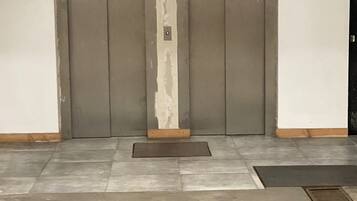Un conjunto de puertas dobles con un cartel vertical, un felpudo y una rejilla metálica en el suelo.