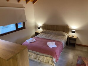 Ein Schlafzimmer mit einem Bett, zwei Nachttischlampen, einem Fenster und einem Holztisch.