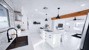 Una cocina moderna con armarios blancos, una isla central, iluminación colgante y una viga de techo de madera.