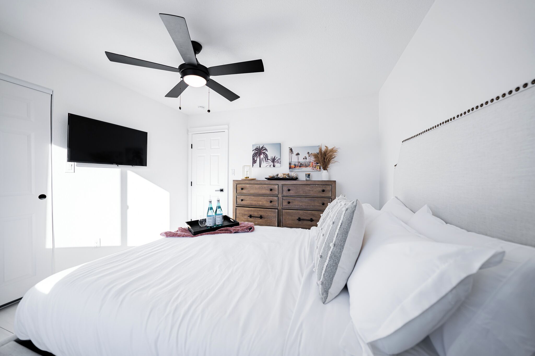 Un dormitorio con cama, ventilador de techo, cómoda, televisor y ventana.