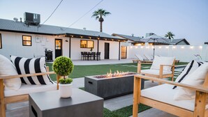Un espacio exterior moderno con sillones de descanso, una chimenea y un comedor.