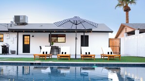Una casa moderna con piscina, mobiliario exterior y un gran paraguas.