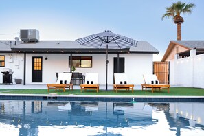 Ein modernes Haus mit Pool, Sitzgelegenheit im Freien und einem großen Sonnenschirm.