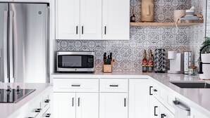 Una cocina moderna con armarios blancos, un refrigerador de acero inoxidable, un microondas y un lavamanos.