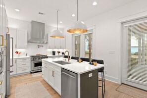 A modern kitchen with stainless steel appliances, a central island, pendant lighting, and a view through large windows. - Sleeps 8 + King Suites + Pool Access | Short Walk to the Sand | Cart & Coast (Santa Rosa Beach)