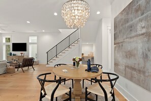 A modern interior with a round wooden table, black chairs, a chandelier, a staircase, and a large abstract painting. - Sleeps 8 + King Suites + Pool Access | Short Walk to the Sand | Cart & Coast (Santa Rosa Beach)