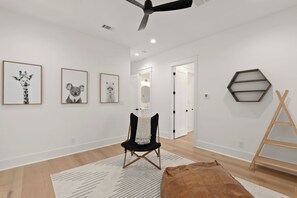 Une pièce dotée d’un ventilateur de plafond, de tableaux représentant des animaux encadrés au mur, d’une chaise noire avec un coussin blanc, d’une échelle en bois et d’un tapis à motifs.