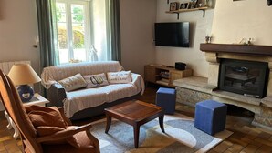 Un salon comprenant un canapé, un fauteuil, une table basse, une cheminée, un téléviseur et des étagères ornées d’objets décoratifs.