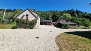 Une propriété rurale avec une allée en gravier, une grande grange et des dépendances plus petites, le tout entouré de verdure et d’arbres.