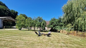 Une cour arrière verdoyante avec un patio couvert, des arbres et une clôture en bois.
