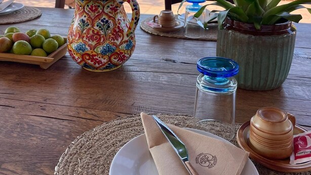 A table set with a plate, napkin, knife, pitcher, potted plant, and a glass jar. - The tranquility of the countryside, just a stone's throw from the sea and the Selinunte Archaeological Park (Sicilia)