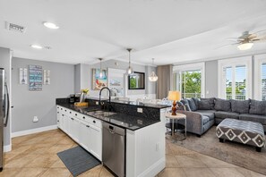 Eine moderne Küche mit einer zentralen Kochinsel, weißen Schränken und einem Essbereich mit einer Couch und Hocker.
