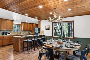 A wooden kitchen with a central island, dining area with chairs, and a chandelier. - Pine-View Big Bear Cabin • Hot Tub + Game Room | London Pines Lodge (Big Bear)