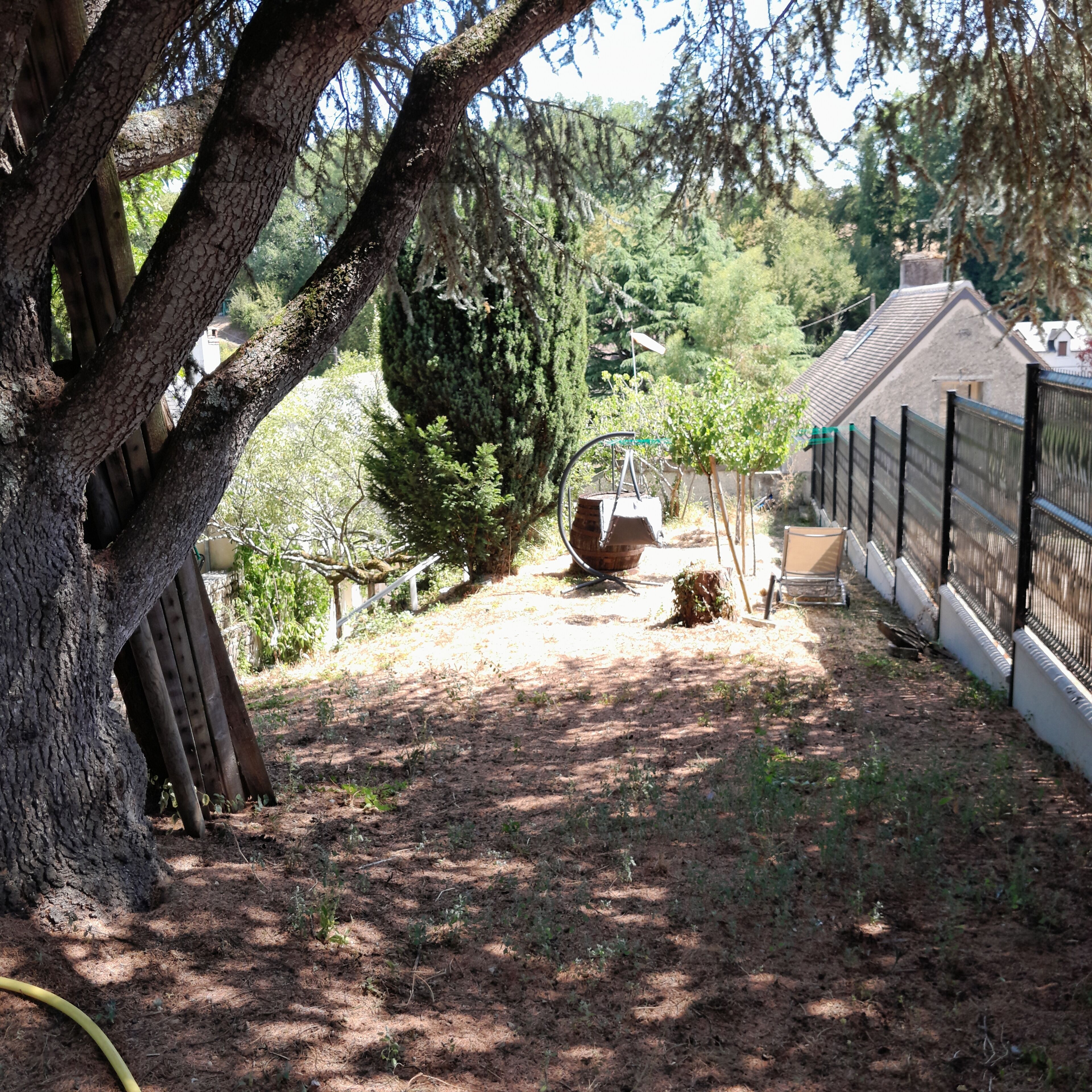 Un espacio exterior cercado con un árbol grande, un columpio y una estructura de ladrillo.
