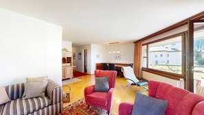 Ein Wohnzimmer mit einer Couch, Sesseln, einem Essbereich mit Tisch und Stühlen sowie einem großen Fenster mit Aussicht.