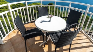 Een balkon met een ronde tafel en vier stoelen, met uitzicht op water en groen.