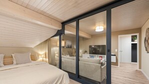Une chambre à coucher comprenant un lit, une porte vitrée donnant sur un espace de vie, un téléviseur et une armoire.