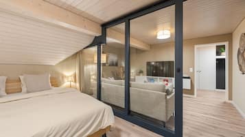 Ein Schlafzimmer mit einem Bett, einer Glastür zu einem Wohnbereich, einem Fernseher und einem Kleiderschrank.