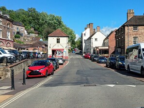 A street lined with parked cars and buildings, including a pharmacy and a toy store.