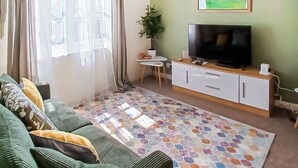 Una sala de estar con un sofá, un televisor, una mesita y una planta en maceta.