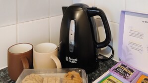 Una encimera de cocina con una tetera, dos tazas, un recipiente con galletas y una caja de bolsitas de té.