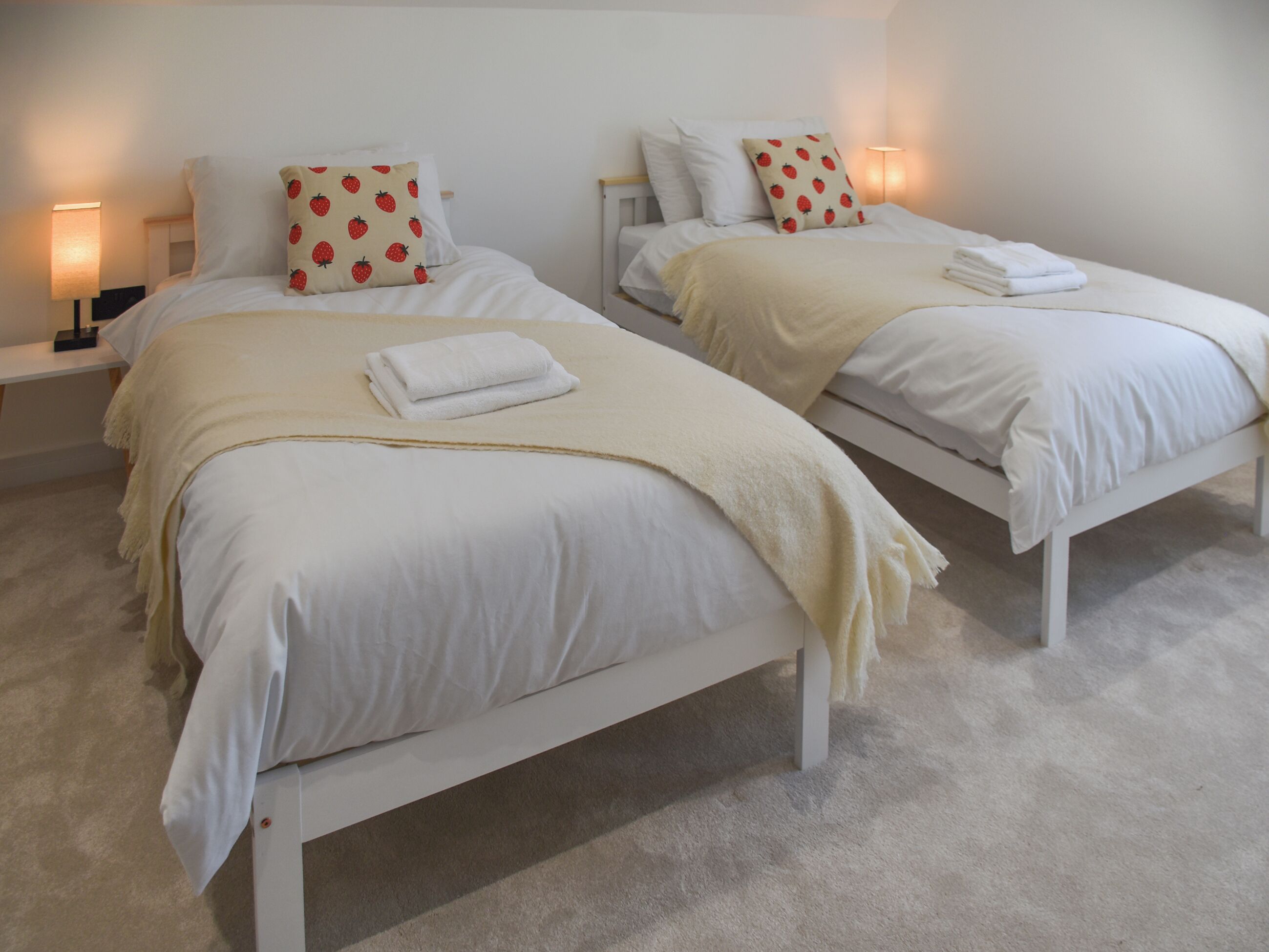 Dos camas individuales con ropa de cama blanca, almohadones estampados de fresas, un plaid beige y una toalla blanca en cada cama.