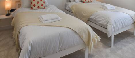 Dos camas individuales con ropa de cama blanca, almohadones estampados de fresas, un plaid beige y una toalla blanca en cada cama.