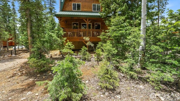 Une cabane en rondins dotée d’un balcon, entourée d’une forêt dense.