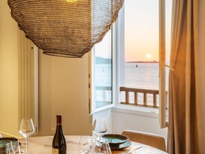 Mesa lista para cenar con una botella de vino, copas y platos, con vistas a un cuerpo de agua al atardecer.