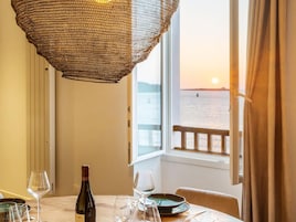 A table set for dining with a bottle of wine, glasses, and plates, overlooking a body of water at sunset.