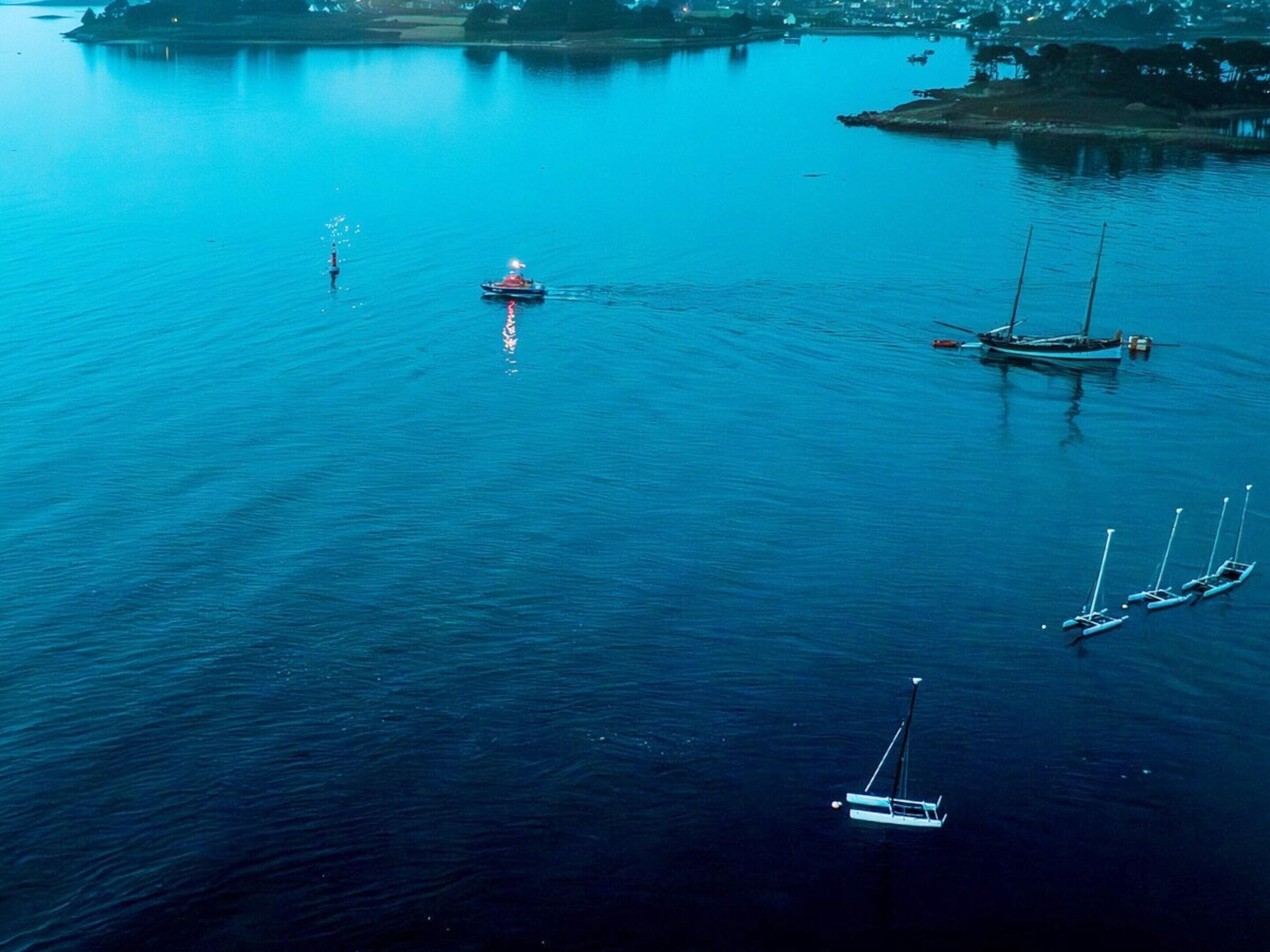 A calm body of water with several boats, including a sailboat and a motorboat.