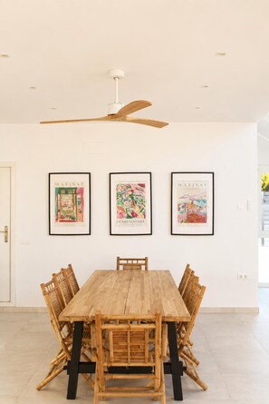 A dining area with a wooden table and chairs, framed artwork on the wall, and a ceiling fan. - Luxury Mediterranean Villa in Roche, Conil, Cádiz. (Roche)