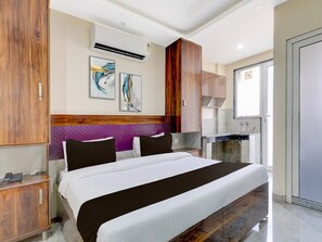 A hotel room with a large bed, wooden wardrobe, two artwork pieces, a kitchenette, and a bathroom. - Deluxetownhouse Phase 3 DLF Cyber City (Gurugram)