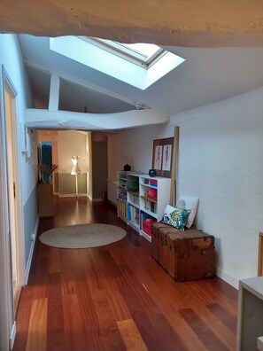 A room with a skylight, wooden flooring, a bookshelf, a suitcase, and a round rug. - House in the heart of the village with a pool, near La Rochelle and Île de Ré (Vérines)