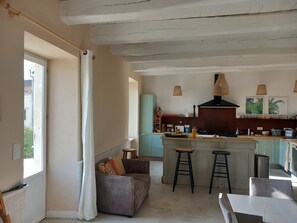A kitchen with a central island, bar stools, a dining table, and a sofa. - House in the heart of the village with a pool, near La Rochelle and Île de Ré (Vérines)