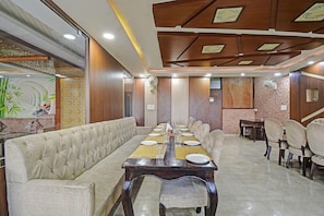 A dining area with a long table set for multiple people, cushioned seating, and a patterned wall. - Townhouse Oak Iskcon Jaipur Formerly Olive Greens (Jaipur)