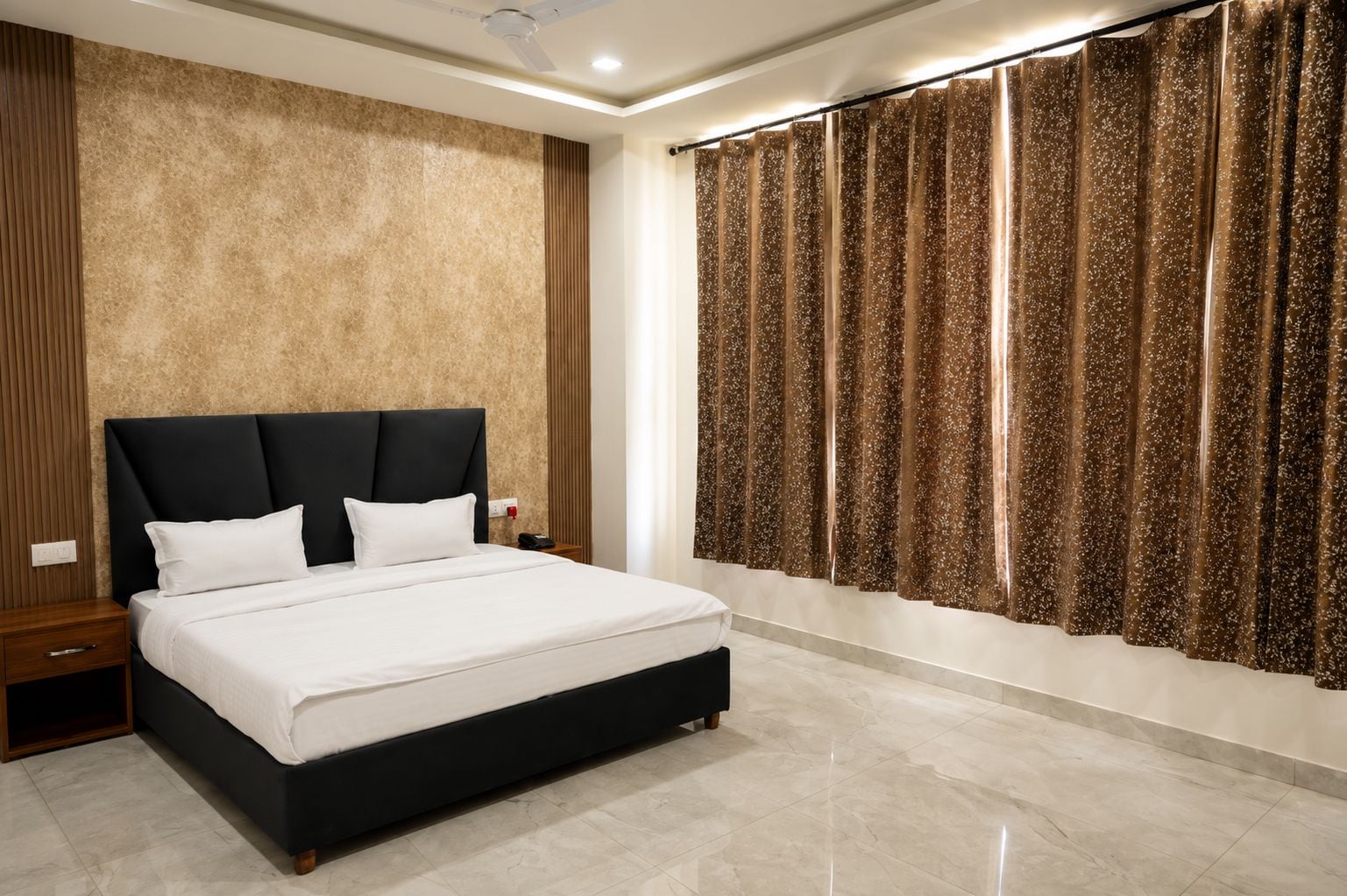 Un dormitorio moderno con una cama grande, una mesita de noche, un teléfono en la pared y una ventana con cortinas estampadas.
